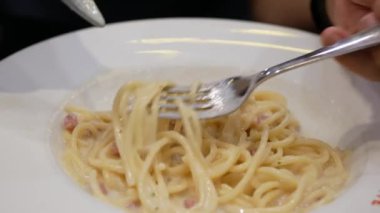 Akşam yemeği için ev yapımı spagetti beyaz soslu makarna yemek için çatal ve kaşık kullanmak, İtalyan mutfağı ev yapımı yemek yemek, kabaralı beyaz soslu makarna yemek.