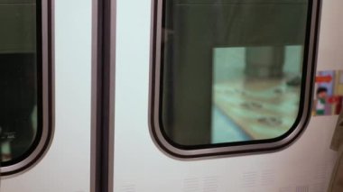 Trenin içindeki banliyö treninin penceresinden, metro metro istasyonundan hareket ederken yoğun saatlerde Japon toplu taşıma arkaplanı görünüyor.