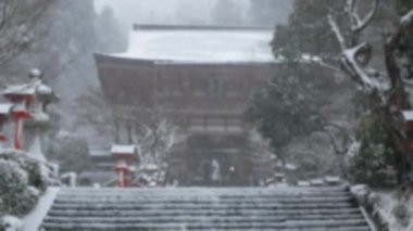 Japon mimari tapınağının ana girişinde bulanık bir görüş açısı var. Kaya merdiven yolu ile giriş kapısına açılıyor. Kış vakti kar yağarken tapınaktaki bazı insanlarla birlikte kar yağıyor.