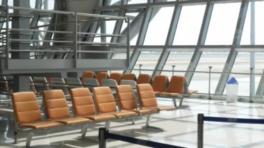Havaalanından çıkış terminalinin içinde bekleme salonundaki bekleme salonunda havaalanının dışında havaalanı manzarası olan havaalanı terminalinde hiç yolcu olmayan bir bank koltuğu var.