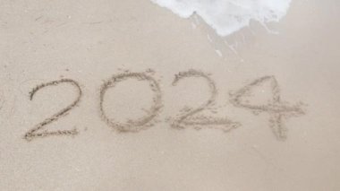 2024 yılı, Tayland 'da beyaz kum yüzey plajında el yazısıyla yazılırken deniz dalgaları sahili vurdu ve 2024 yılını sildi. 2025 yılını kutlamaya hazır, plajda yeni yıl metni 2024