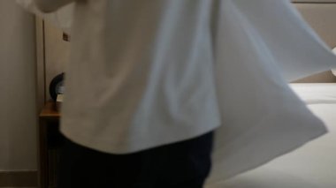 Asyalı erkek temizlikçi yatak temizliği battaniye düzenleme, yastıklar ve yatak odaları kurmak sabah uyandıktan sonra dinlenme tesisinde yatak odası temizlemek misafir girişine hazır.