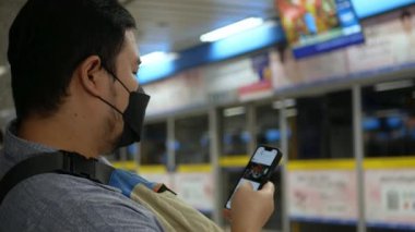 Asyalı genç adam metro istasyonunda gelişini beklerken internet sosyal medyasında 5 gramlık akıllı telefon kullanıyor.