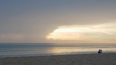 Günbatımı saatinde deniz plajı yüzeyinde dramatik bir gün batımı. Akşam gökyüzünde birçok bulut. Dalgalar altın kum sahiline çarpıyor.