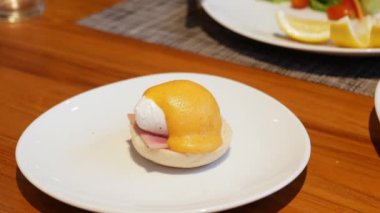 Bıçak ve çatal kullanarak yumurta sarısı keserek İngiliz usulü yumurtalı çöreği beyaz tabakta fenerle yiyorlar. Sağlıklı kahvaltı yemeği için yumurta sarısı ve kızarmış ekmek..