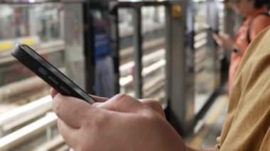 Bir adamın elini tutarken akıllı telefon kullanarak sohbet ederken yaz günü perona yaklaşan trenin tren istasyonunu beklerken, şehir hayatı tren beklerken cep telefonu kullanıyor.