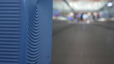 Havalimanı kalkış terminalinde yolculuk için kalkış kapısına doğru ilerlerken hareket halindeki yürüyen yürüyen merdivene odaklı seçici bir bavul.