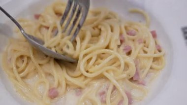 Akşam yemeği için ev yapımı spagetti beyaz soslu makarna yemek için çatal ve kaşık kullanmak, İtalyan mutfağı ev yapımı yemek yemek, kabaralı beyaz soslu makarna yemek.