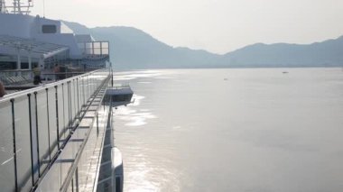 Kıç bölgesinden ileri doğru ilerleyen devasa lüks yolcu gemisinin üst güvertesinde, güneş doğarken yavaş yavaş körfeze doğru yelken açarken görüntüsü.