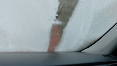 Soğuk bir kış sabahı adamın biri arabasının ön camını çiziyor.