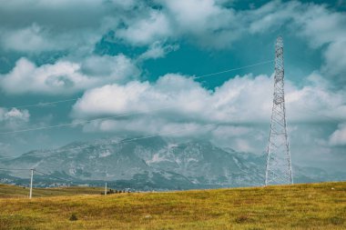 Arka planda dağlar olan yüksek voltajlı elektrik hattı