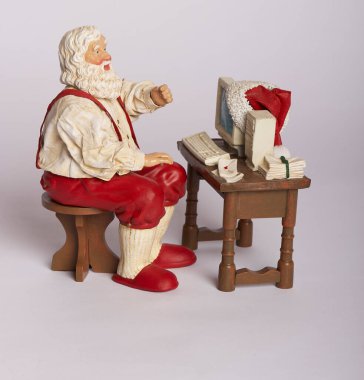 santa claus figurine sitting at desk working on computer making children's gift list for christmas clipart