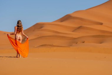 Güzel bir model, Fas 'taki büyük Sahra Çölü' ndeki kum tepelerine çıplak poz veriyor.