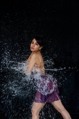 Makyajlı ve su sıçratan genç Latin kadının fotoğrafı. Yüzünde su damlaları olan Latin bikinili kadının portresi. Moda modeli ve su. Moda konsepti.