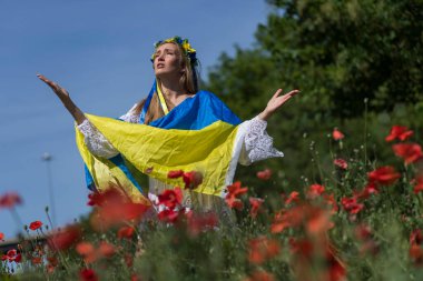 Ukraynalı genç sarışın bir kadın elinde Ukrayna bayrağıyla kırmızı gelincik tarlasında duruyor ve memleketi Ukrayna 'daki savaşa verdiği desteği gösteriyor.
