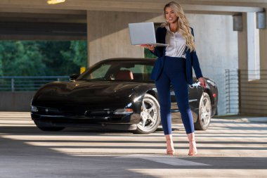 Muhteşem sarışın bir model spor arabasını kullanmadan önce bilgisayarında çalışıyor.