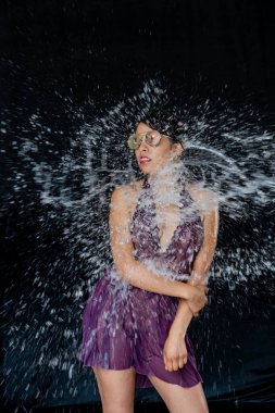 Makyajlı ve su sıçratan genç Latin kadının fotoğrafı. Yüzünde su damlaları olan Latin bikinili kadının portresi. Moda modeli ve su. Moda konsepti.