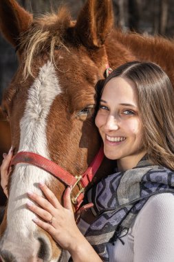 A beautiful brunette cowgirl poses with her horse before a ride in the countryside