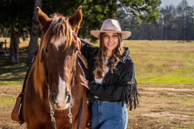 A beautiful brunette cowgirl poses with her horse before a ride in the countryside