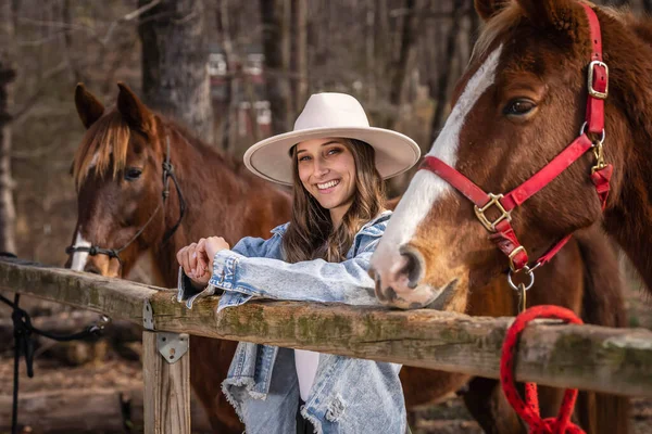 A beautiful brunette cowgirl poses with her horse before a ride in the countryside