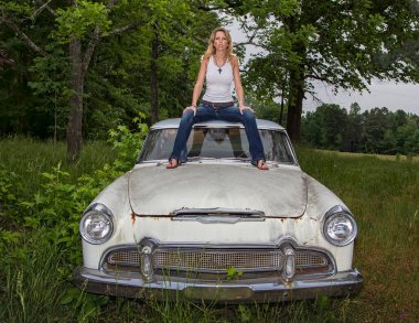 A gorgeous model poses with an old worn out vehicle outdoors