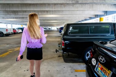 Muhteşem sarışın bir model başarılı bir toplantıdan sonra kapalı otoparkta arabasına doğru yürür.