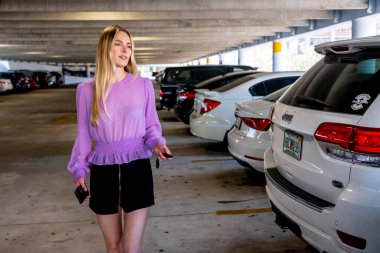 Muhteşem sarışın bir model başarılı bir toplantıdan sonra kapalı otoparkta arabasına doğru yürür.