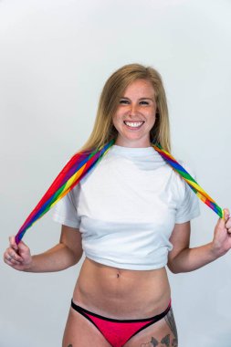 Studio image of happy young blonde LBGTQ woman wearing rainbow colored clothes smiling at camera.  Concept of homophobia, diversity, equity, peace and love, freedom, liberty. LGBT rights concept.  