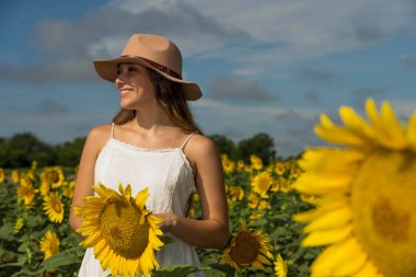 A gorgeous blonde model poses outdoors in a field of sunflowers