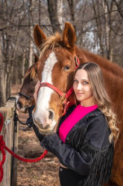 A beautiful brunette cowgirl poses with her horse before a ride in the countryside