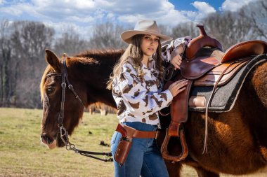 A beautiful brunette cowgirl poses with her horse before riding in the country