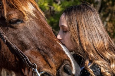 A beautiful brunette cowgirl poses with her horse before a ride in the countryside