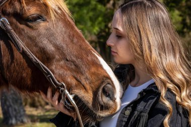 A beautiful brunette cowgirl poses with her horse before a ride in the countryside