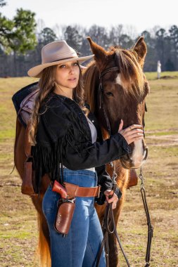 A beautiful brunette cowgirl poses with her horse before riding in the country