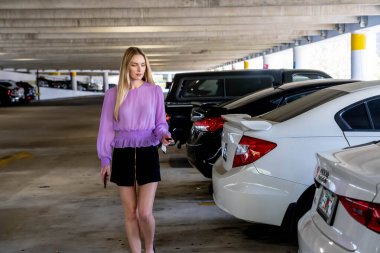 Muhteşem sarışın bir model başarılı bir toplantıdan sonra kapalı otoparkta arabasına doğru yürür.