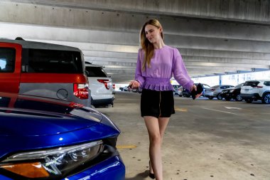 Muhteşem sarışın bir model başarılı bir toplantıdan sonra kapalı otoparkta arabasına doğru yürür.