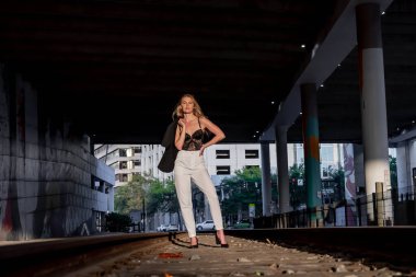 Sarışın bir model gün batımında tren raylarında poz veriyor.