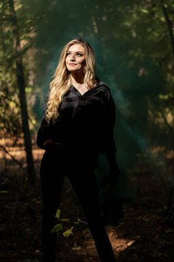 Muhteşem sarışın bir model, kasvetli bir orman ortamında poz veriyor.