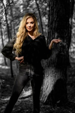 Muhteşem sarışın bir model, kasvetli bir orman ortamında poz veriyor.