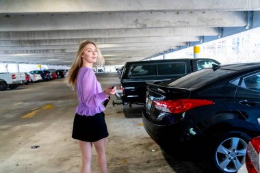 Muhteşem sarışın bir model başarılı bir toplantıdan sonra kapalı otoparkta arabasına doğru yürür.