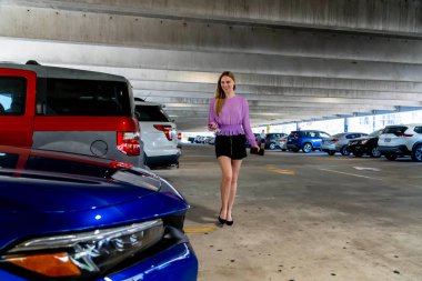Muhteşem sarışın bir model başarılı bir toplantıdan sonra kapalı otoparkta arabasına doğru yürür.