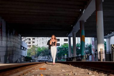 Sarışın bir model gün batımında tren raylarında poz veriyor.