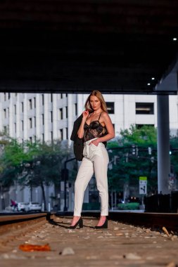 Sarışın bir model gün batımında tren raylarında poz veriyor.