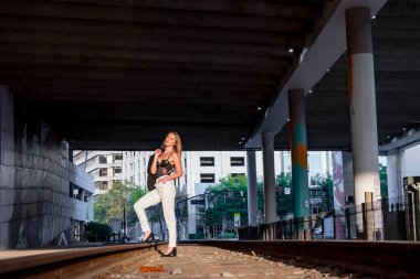 Sarışın bir model gün batımında tren raylarında poz veriyor.