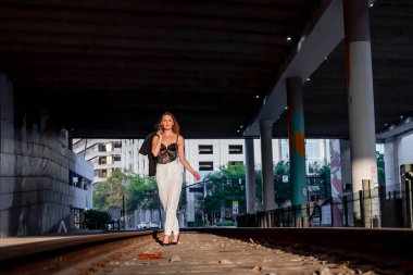 Sarışın bir model gün batımında tren raylarında poz veriyor.