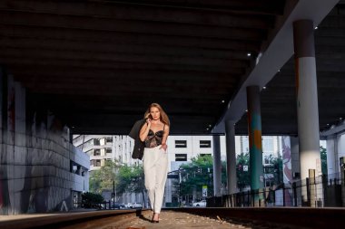 Sarışın bir model gün batımında tren raylarında poz veriyor.