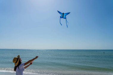Güzel, olgun bir esmer model sahilde uçurtmasını uçururken günün tadını çıkarıyor.