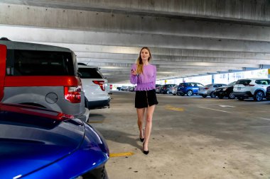 Muhteşem sarışın bir model başarılı bir toplantıdan sonra kapalı otoparkta arabasına doğru yürür.