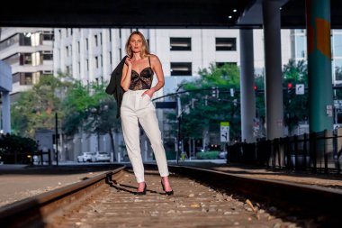 Sarışın bir model gün batımında tren raylarında poz veriyor.