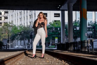 Sarışın bir model gün batımında tren raylarında poz veriyor.